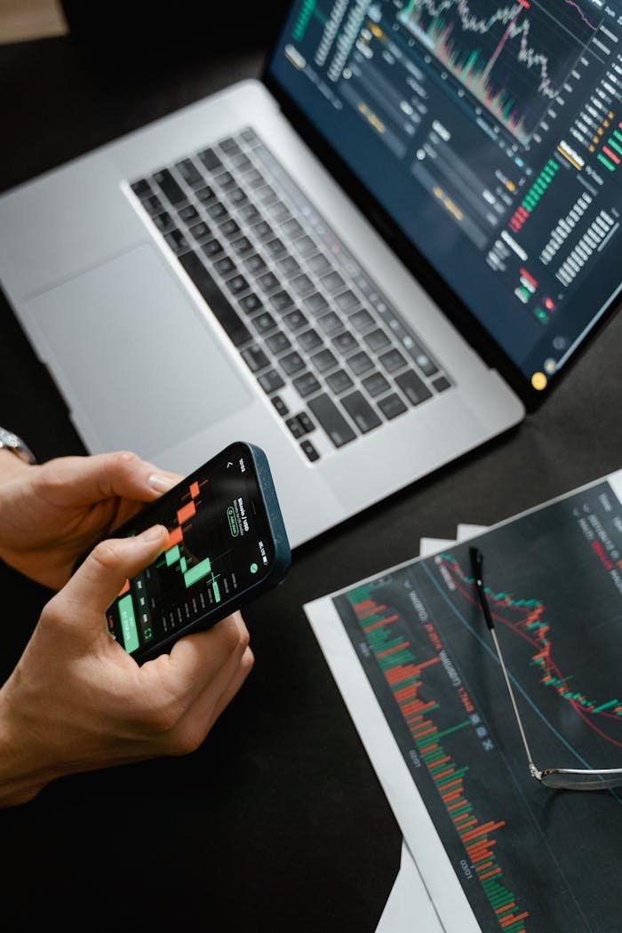 about-us-01 Hands holding phone with financial graph, laptop in view.