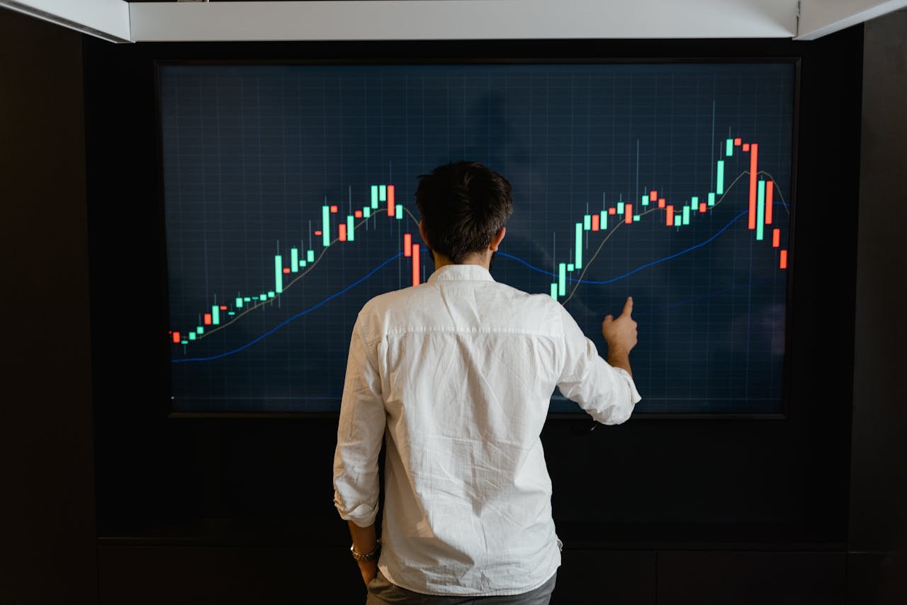 heros-img Adult male reviewing stock market data on a large display screen indoors.
